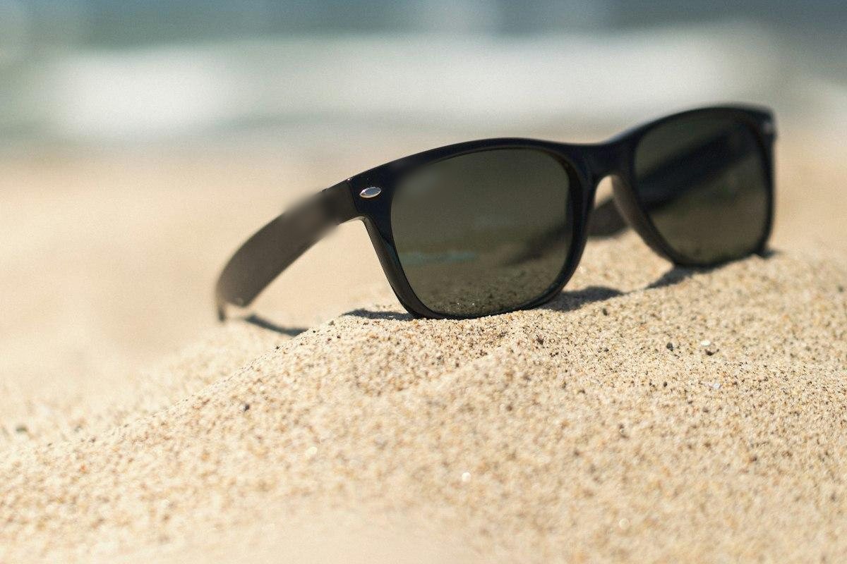 A pair of black sunglasses resting on beach sand