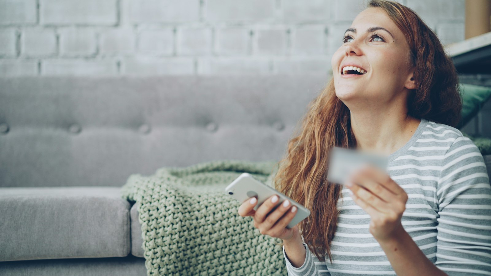 A happy young woman shopping online on her phone at home